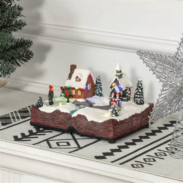 Animated Christmas village decoration with lit houses and snow on an open book base
