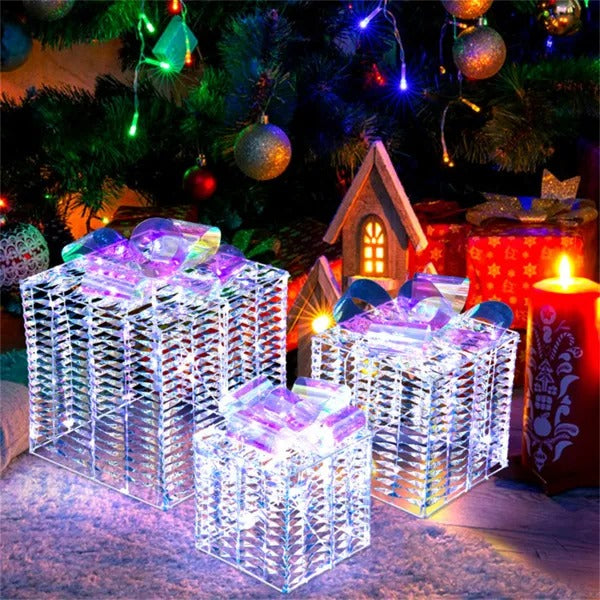 Set of three iridescent lighted Christmas gift boxes under decorated Christmas tree with ornaments and candle
