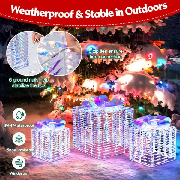 Set of three iridescent lighted Christmas gift boxes outdoors in snow under decorated tree, weatherproof and stable