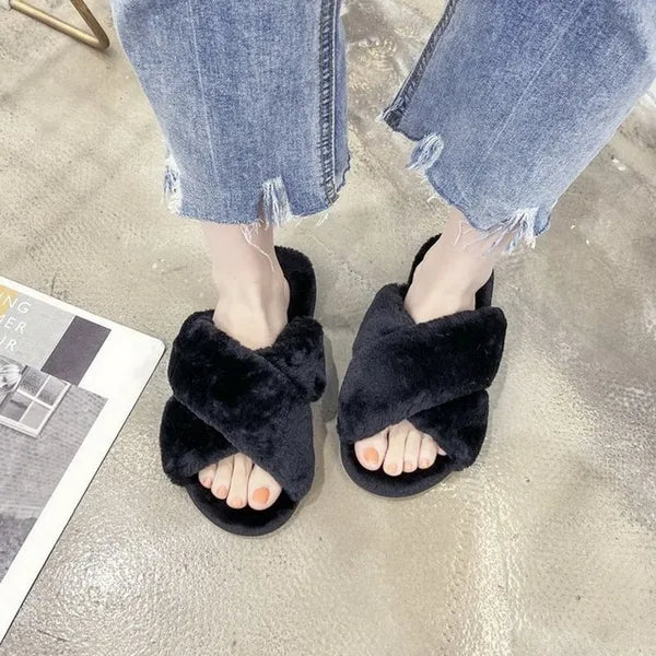 person wearing black faux fur slippers with crisscross design and frayed hem blue jeans on concrete floor