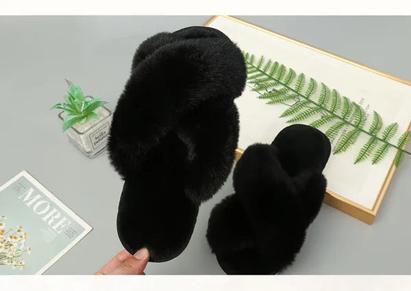 Pair of black faux fur slippers with cozy crossed straps on grey surface with plant and book