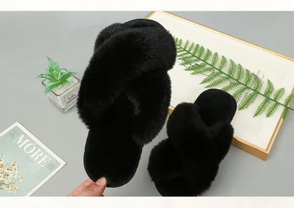 Pair of black faux fur slippers with cozy crossed straps on grey surface with plant and book
