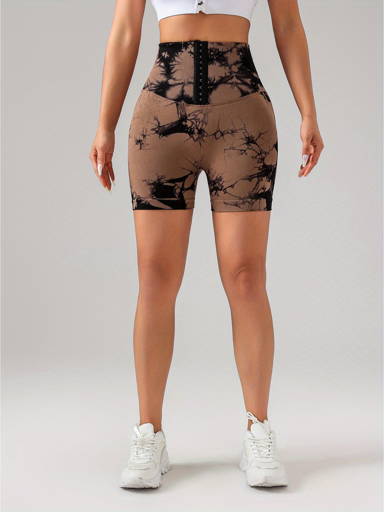 Woman wearing high waist black and brown tie-dye scrunch butt lifting shorts with white sneakers