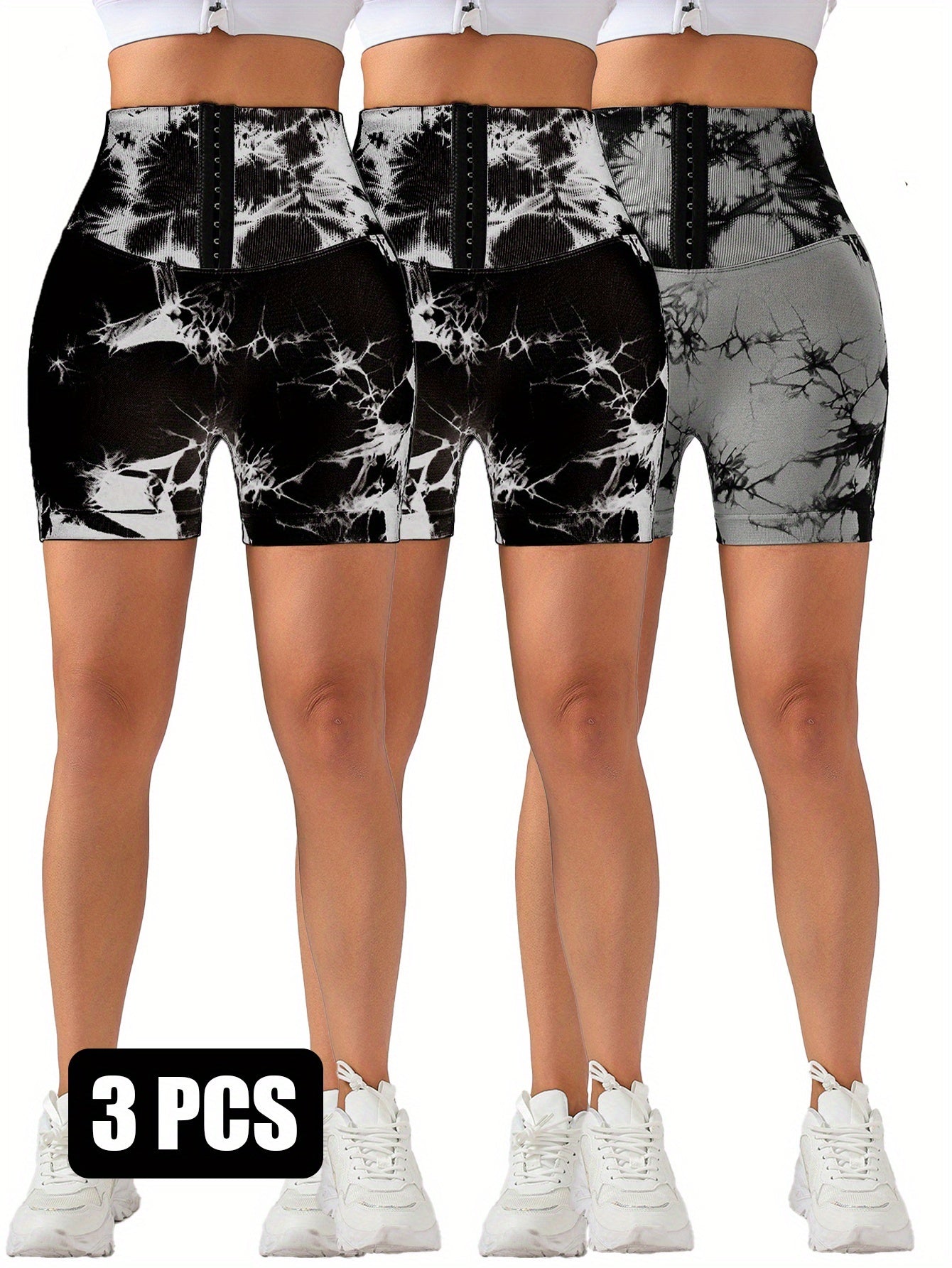 Three pairs of high-waisted tie-dye compression shorts with hook-and-eye front in black and gray shades, worn with white sneakers