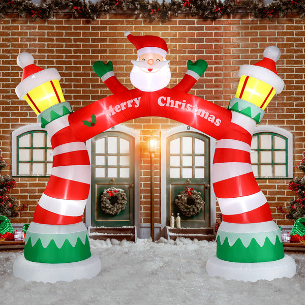 Inflatable Christmas arch with Santa figure, red and white stripes, and yellow lanterns in snowy festive scene
