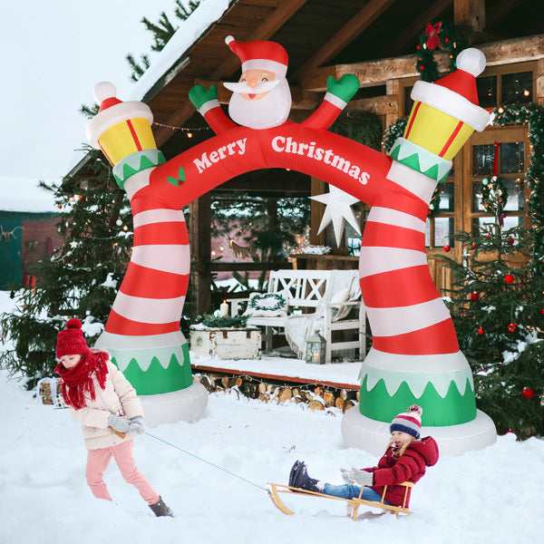 Inflatable Christmas arch with Santa and striped lanterns in snowy yard, kids playing with sled