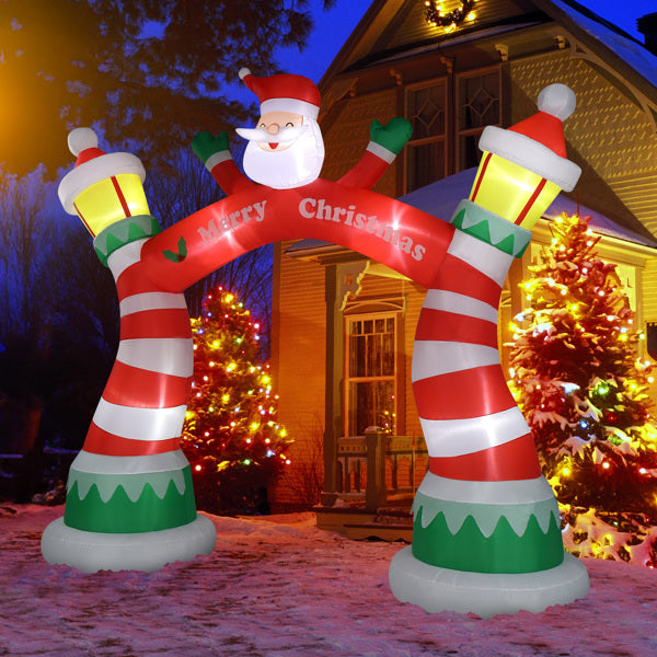 Inflatable Christmas arch with Santa and candy cane stripes, lit at night with decorated trees
