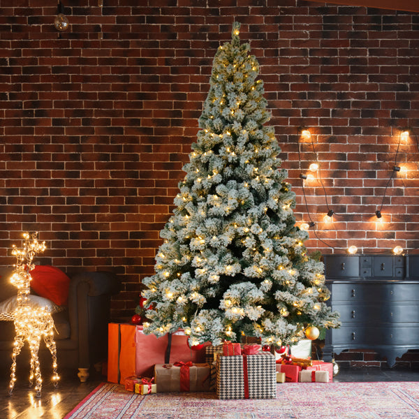 6ft flocked Christmas tree with warm white lights and wrapped gifts against a brick wall