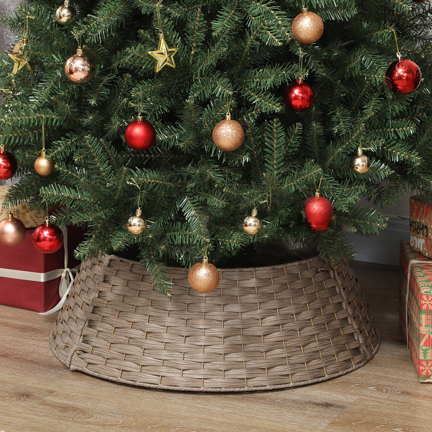Christmas tree with red and gold ornaments standing on wicker tree collar on wooden floor