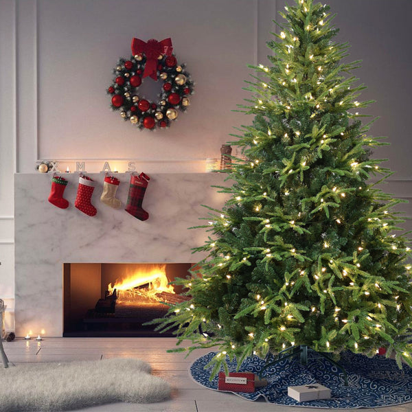 5ft green artificial Christmas tree with warm white LED lights by a lit fireplace with stockings and a red and gold wreath