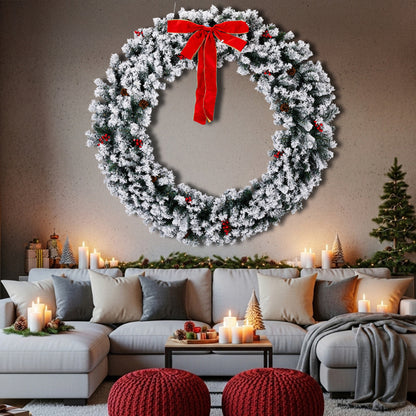 Large snow-flocked Christmas wreath with red bow and berries above cozy living room with candles and festive decor