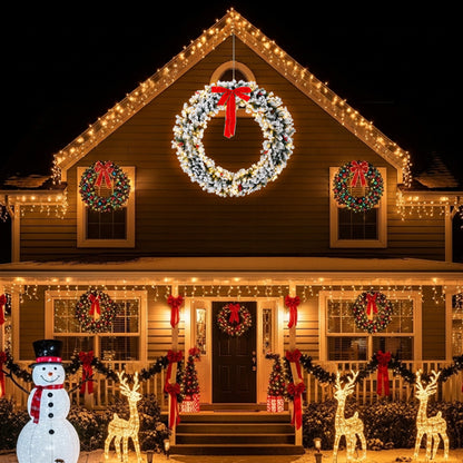 Snow-flocked Christmas wreath with warm white LED lights and red bow on house with festive holiday decorations