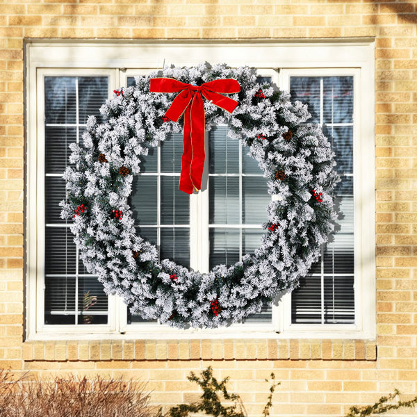 60-inch snow flocked Christmas wreath with red bow and berries on a house window