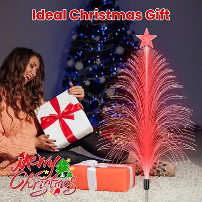 Woman opening Christmas gift near pink fiber optic cedar tree light and decorated blue Christmas tree