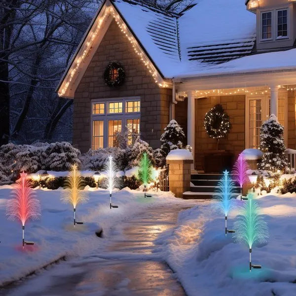 Snow-covered house decorated with warm string lights, wreaths, and colorful solar fiber optic cedar tree lights along the walkway