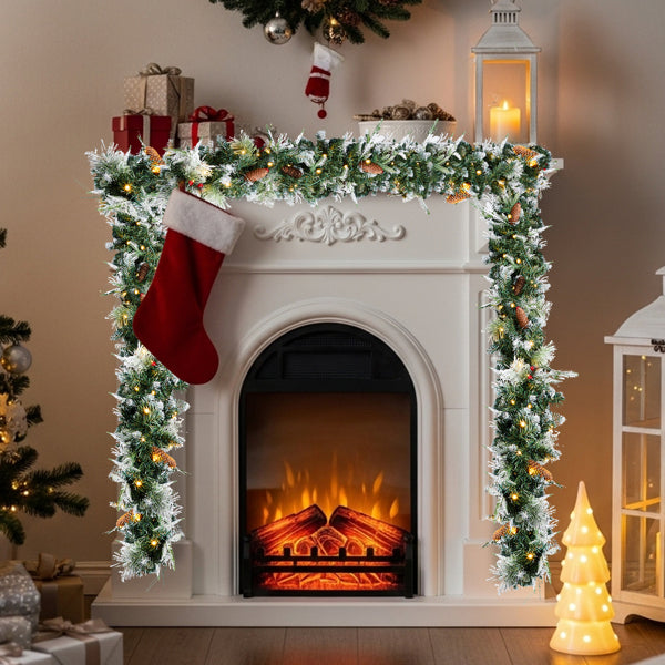 Snow-flocked Christmas garland with warm lights framing a white fireplace with a red stocking and glowing fire