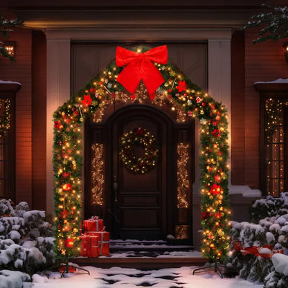 Christmas garland archway with red bow and lights framing a front door with wreath and snow-covered bushes