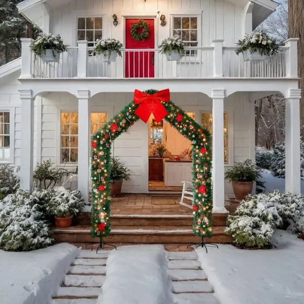 Snowy white house with red door and decorated Christmas artificial tree archway featuring lights and red bow