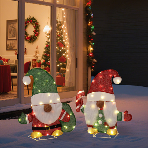 Outdoor Christmas decorations featuring two lighted gnome figures with candy cane and festive hats on snowy patio
