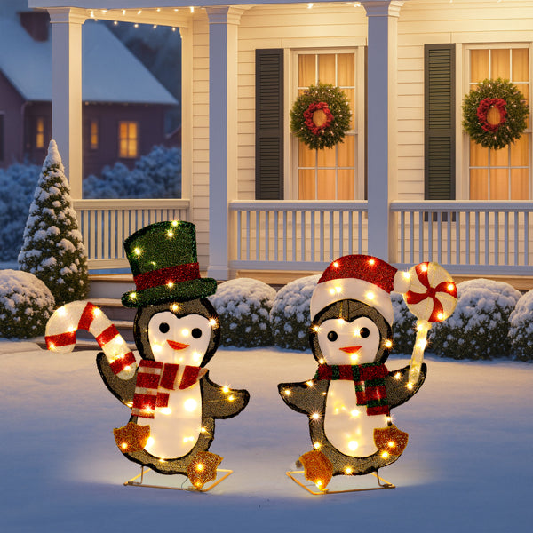 Lighted Christmas penguin decorations with candy canes, scarves, and hats on snowy porch