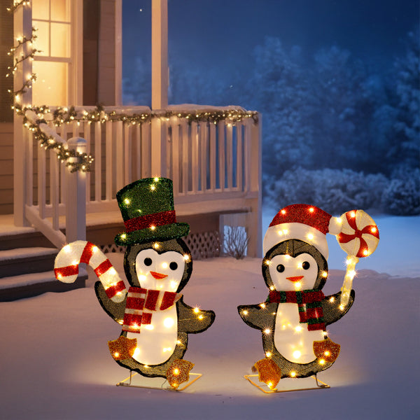 Lighted Christmas penguin yard decorations with candy canes, scarves, and hats on snowy porch