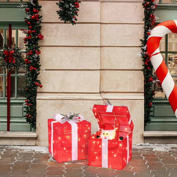 Outdoor Christmas scene with illuminated red gift boxes and a Santa figure inside one box, festive garlands
