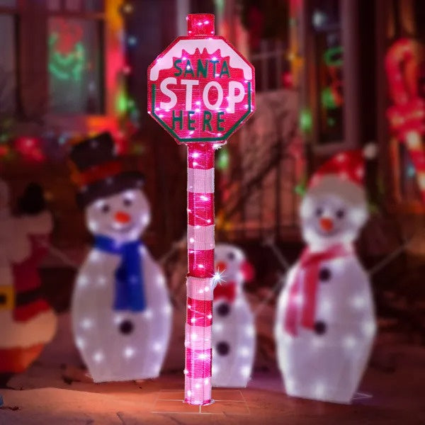 LED lighted Santa Stop Here sign in front yard with illuminated snowman decorations at night