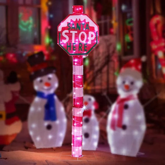 LED lighted Santa Stop Here sign in front yard with illuminated snowman decorations at night