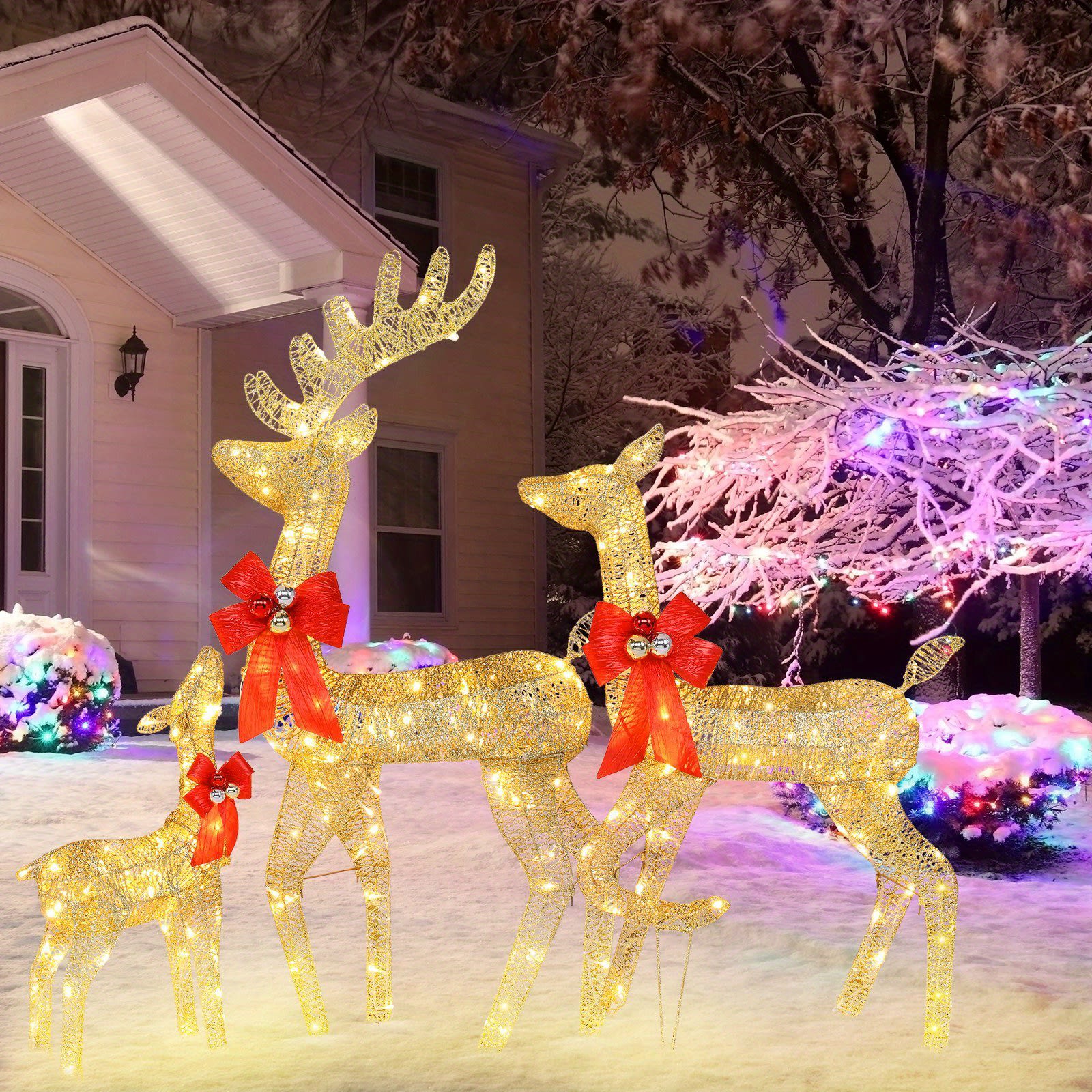 Outdoor Christmas scene with golden light-up reindeer family decoration wearing red bows in snowy yard