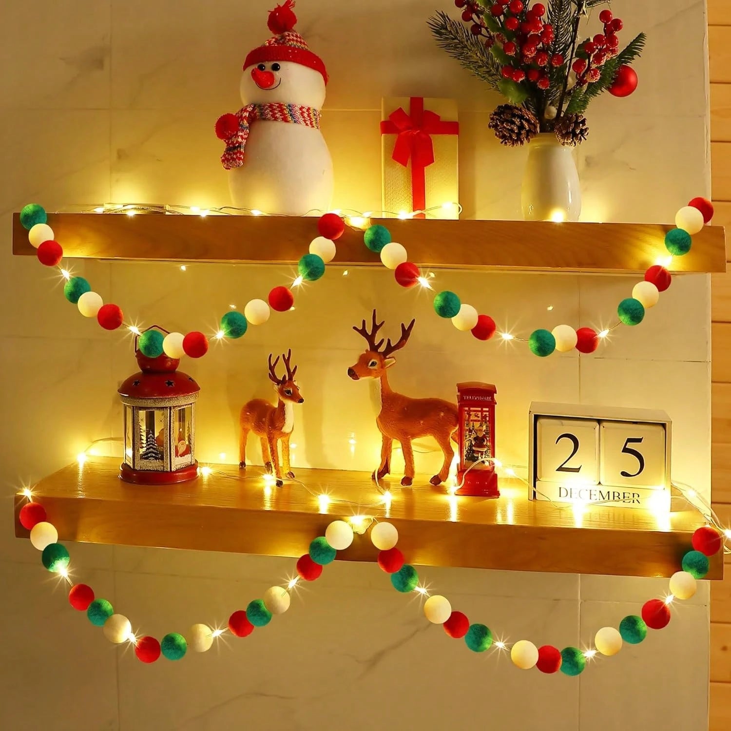 Christmas decorations on wooden shelves with snowman, deer, gift, lights, and red-green-white pom-pom garland