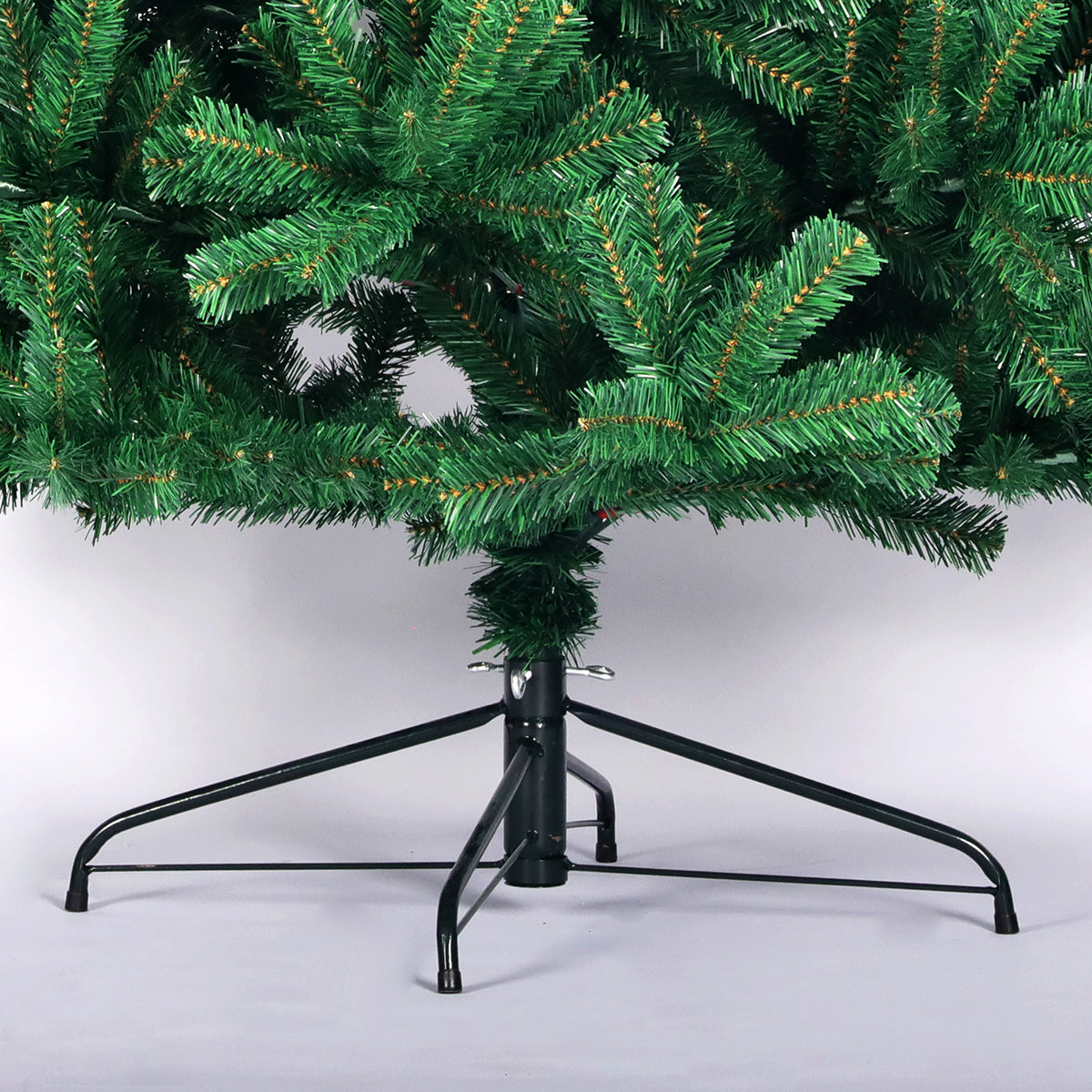 Close-up of green artificial spruce Christmas tree branches and black foldable metal stand on white background