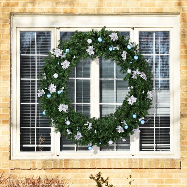 Large green Christmas wreath with silver poinsettias and blue and white ornaments on a window