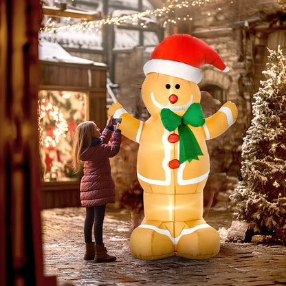 Big inflatable gingerbread man with LED lights wearing Santa hat and green bow, girl taking photo in snowy courtyard