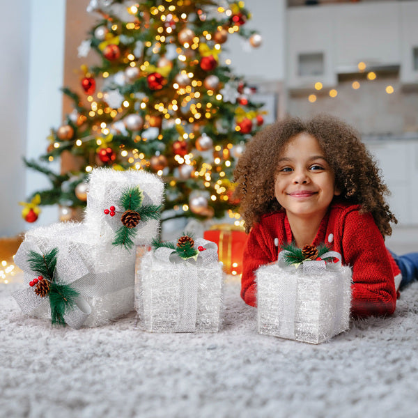 Smiling child in red sweater lying on carpet near glittery Christmas gift boxes with pinecone decor by decorated tree