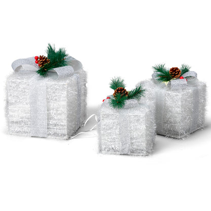 Set of three white lighted Christmas gift boxes decorated with silver ribbons, pine cones, and green pine sprigs