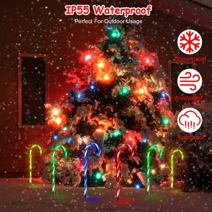 Snow-covered outdoor Christmas tree with multicolor lights and six glowing candy cane stake lights in snow