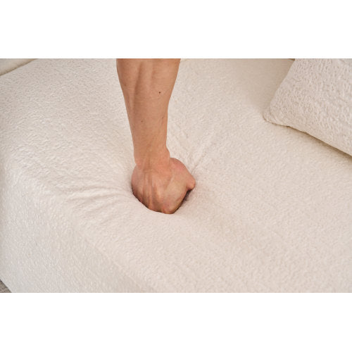 Hand pressing into soft beige textured fabric cushion of a modern plush sofa