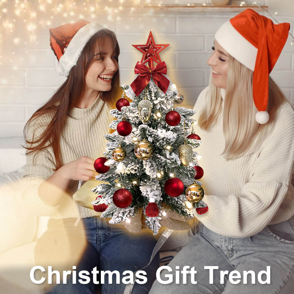Two women in Santa hats decorating a small flocked Christmas tree with red and gold ornaments
