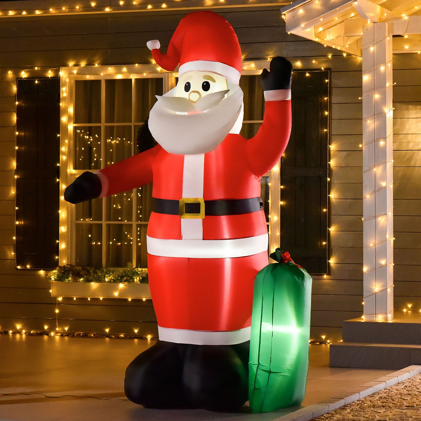 Inflatable Santa Claus decoration with red suit and green sack, lit up outside house with Christmas lights