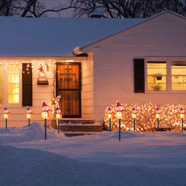 Snow-covered house decorated with warm white LED snowman stake lights and icicle string lights at night