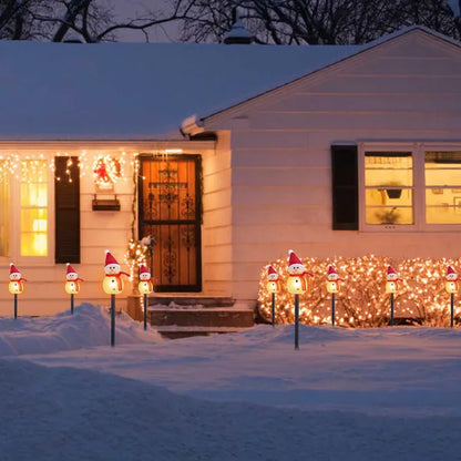 Snow-covered house decorated with warm white LED snowman stake lights and icicle string lights at night