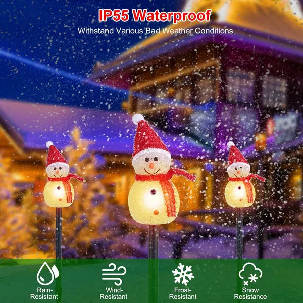 Three illuminated snowman stake lights with red hats and scarves in snowy yard at night, IP55 waterproof