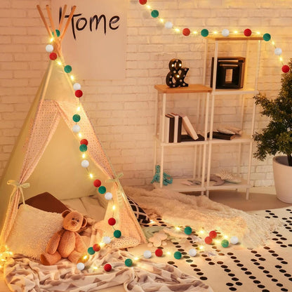 Cozy kids playroom with teepee tent, teddy bear, warm white string lights, and red-green-white felt ball garland