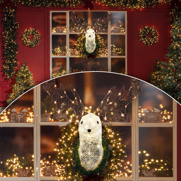 Lighted reindeer head with warm white LED lights mounted on a wreath on a festive red wall with Christmas wreaths and garlands