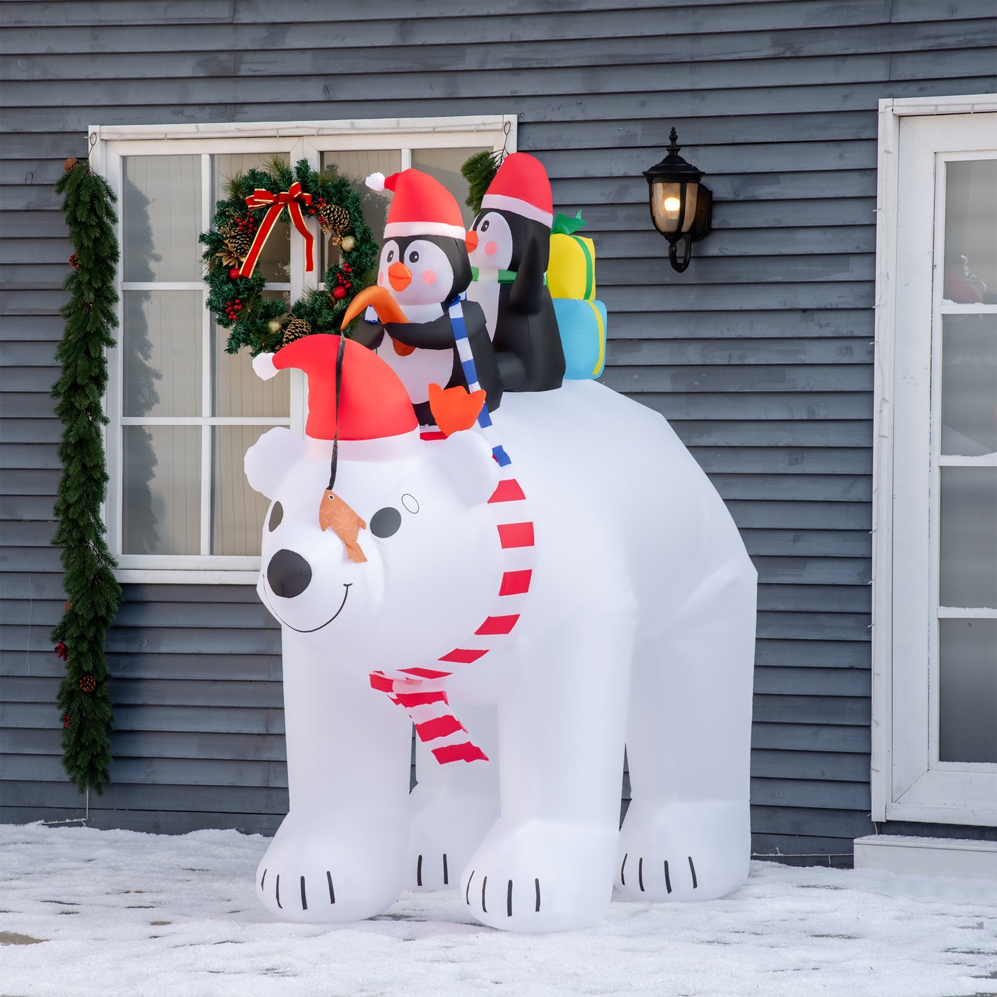 Outdoor inflatable Christmas decoration of polar bear with red scarf wearing Santa hat carrying two penguins and gifts