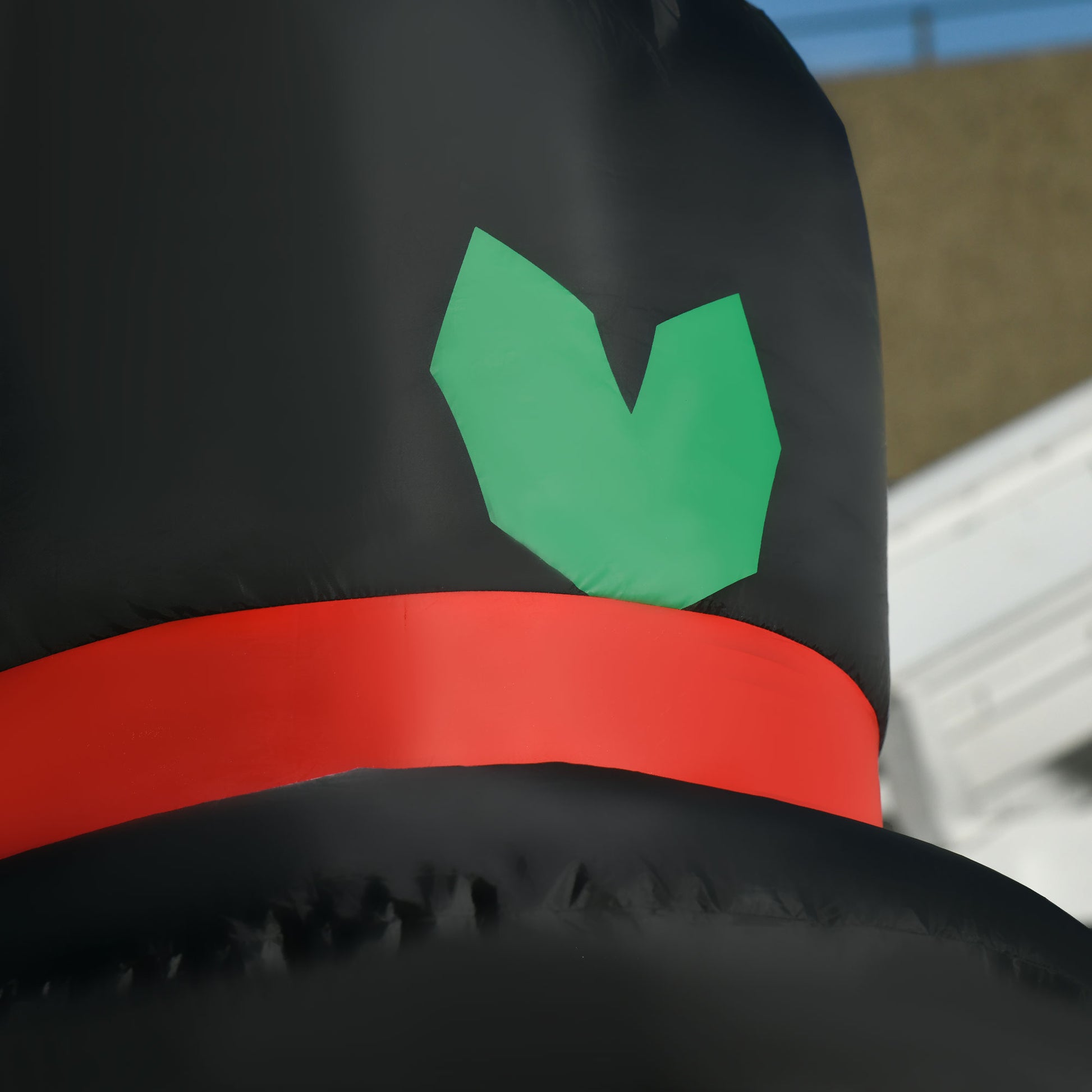 Close-up of inflatable snowman black top hat with red band and green holly decoration outdoors