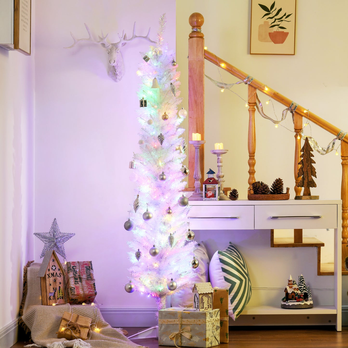 Slim white pencil Christmas tree with LED lights and silver ornaments in cozy living room under wooden stairs