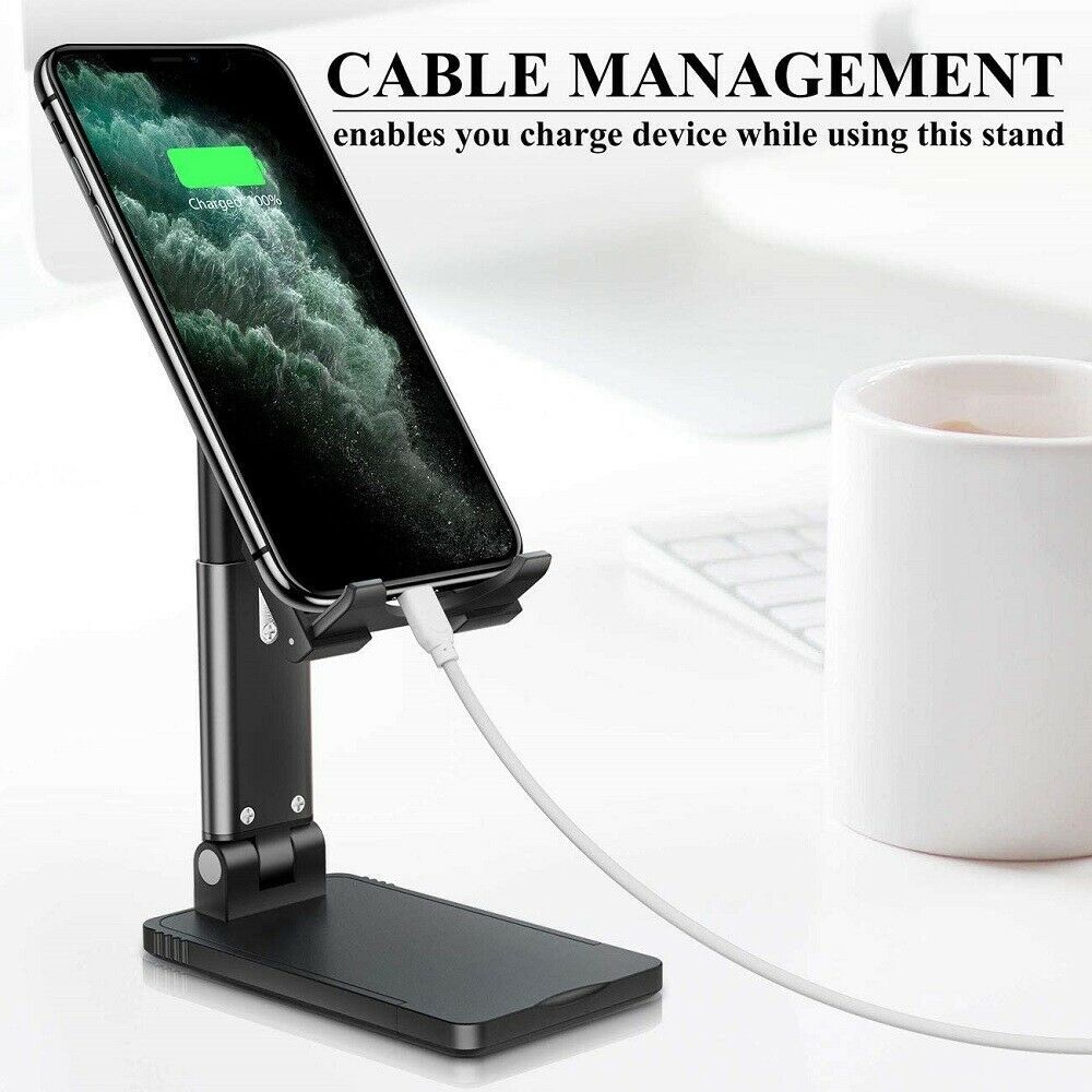 Black adjustable foldable phone stand holding a charging smartphone with cable management feature on a white desk