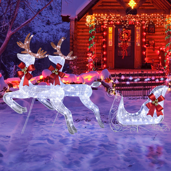 LED white reindeer and sleigh Christmas yard decoration with red bows in snowy yard at night