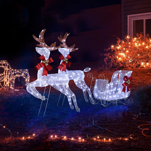 White LED lighted reindeer and sleigh yard decoration with red bows and bells at night